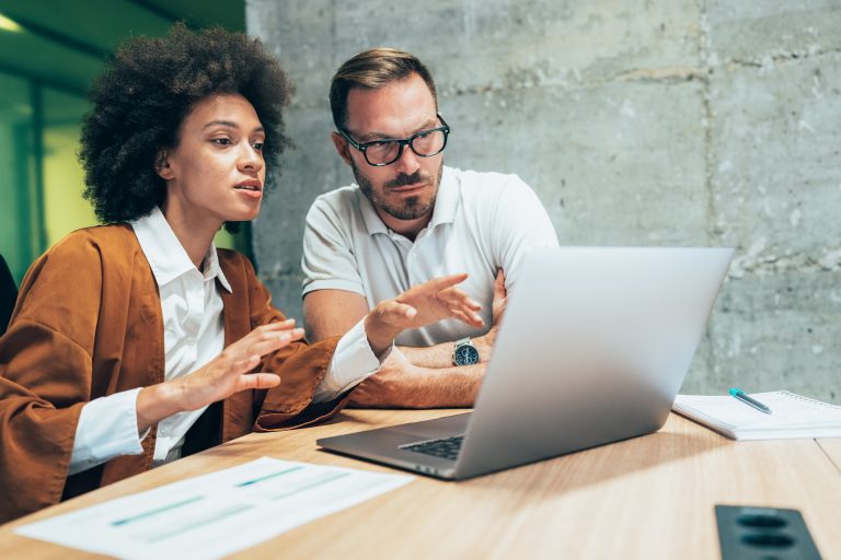 One man and one woman worker reading off a laptop in a meeting